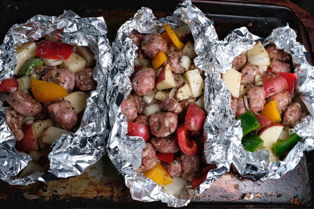 Sausage, potatoes, and peppers wrapped in foil on a baking sheet.