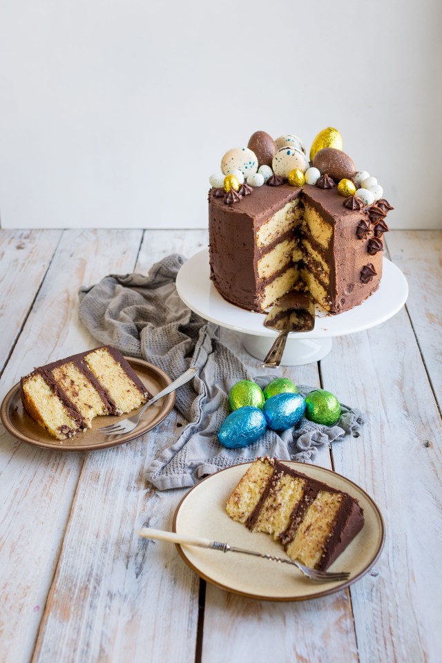 an image of a  sliced moist vanilla layer cake topped with chocolate eggs and macarons, with slices in a plate 

